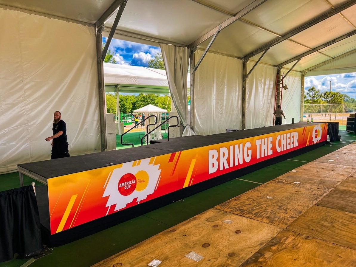 wide shot of a completed outdoor event stage with tent flooring on a manicured venue lawn, showing the full setup with stairs and skirting
