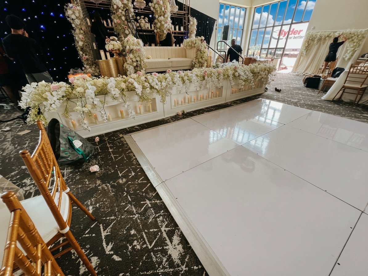 white dancefloor adjacent to a skirted rectangular stage at an evening wedding reception with uplighting