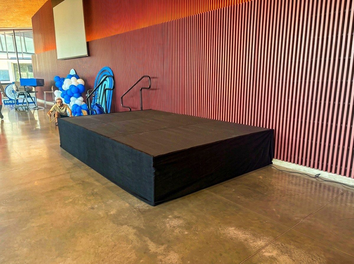 event stage setup integrated with decorative balloon marquee display, showing stage platform with tent flooring and large balloon arch installation at an outdoor venue