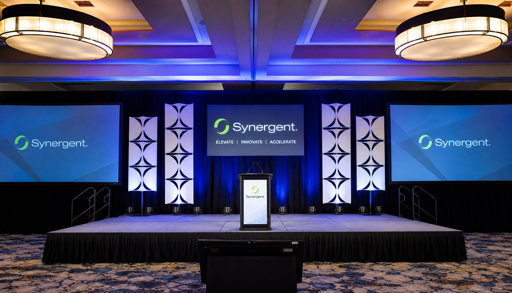 stage setup inside a hotel ballroom with pipe and drape backdrop and corporate event lighting